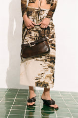 Espresso-brown shoulder bag worn by person, front buckle and crossbody strap.