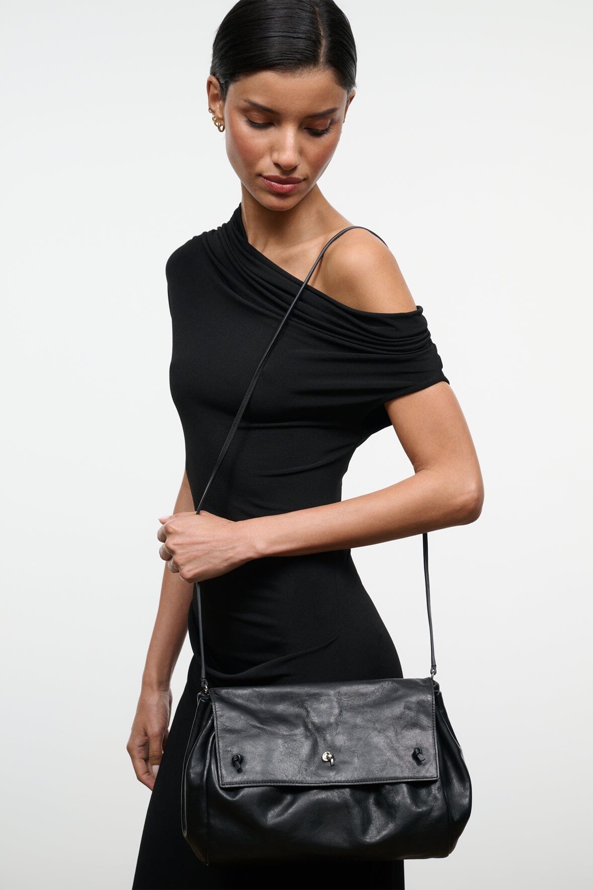 Black convertible shoulder bag with ruched top and front flap, worn with long strap