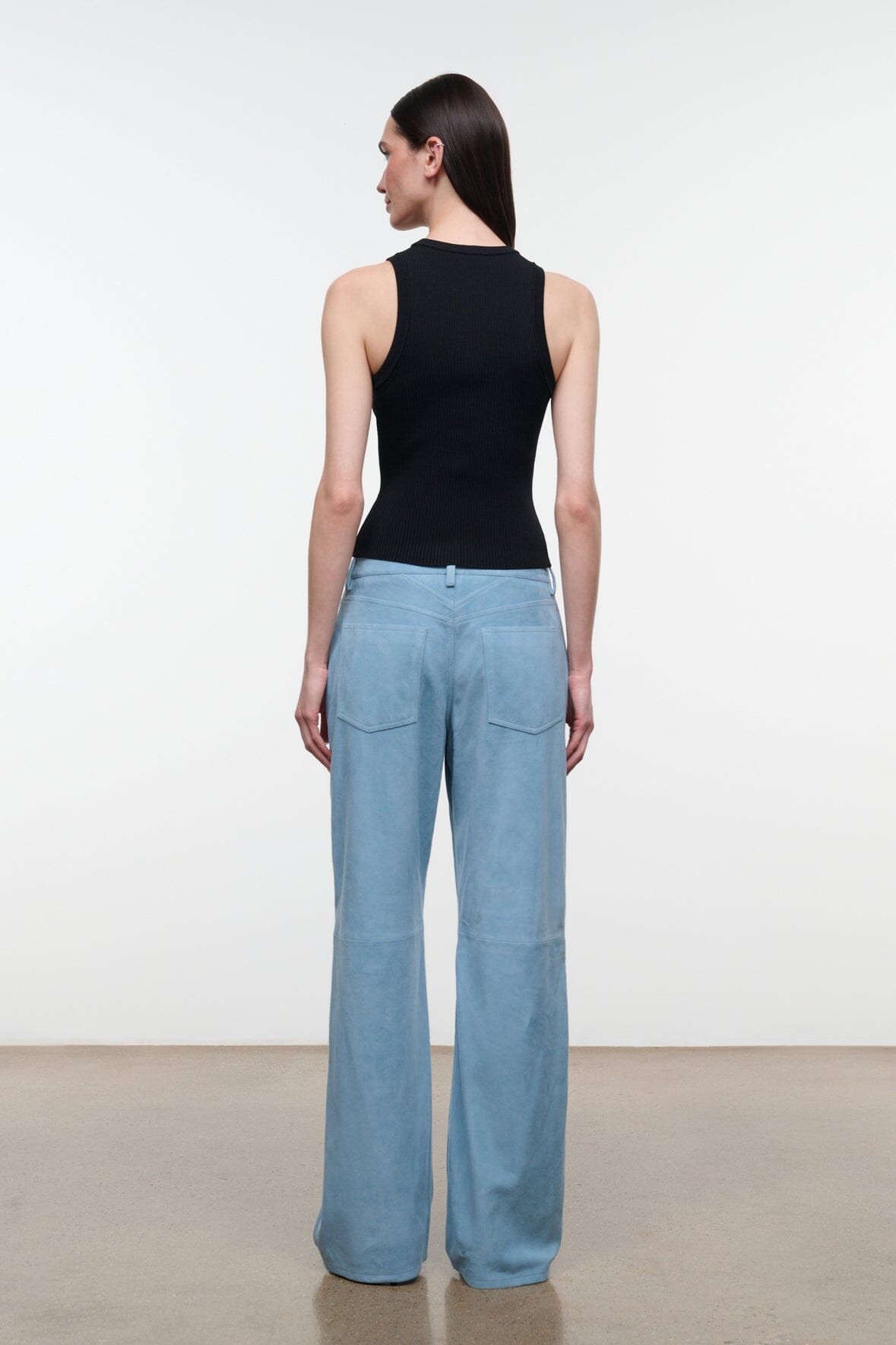 Sky blue suede pants viewed from the back, with patch pockets and wide legs.