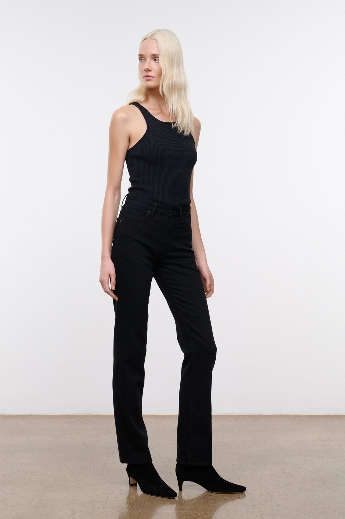 Black straight jeans on model, with button fly, belt loops, and back yoke pockets