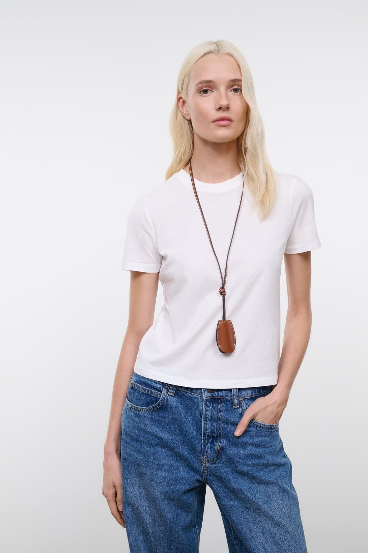 Tan-brown leather whistle pendant on cord worn with a white T-shirt