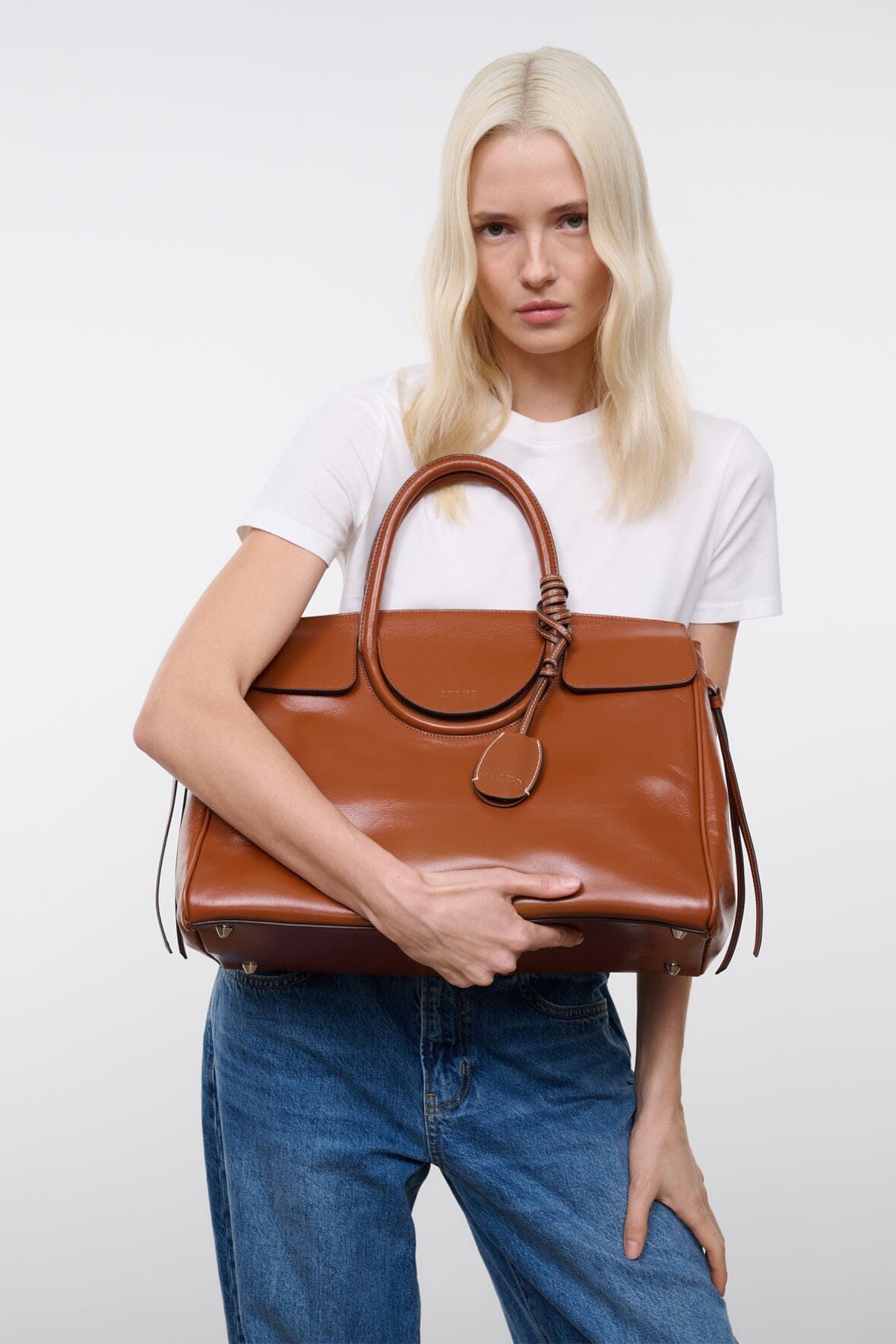 Tan-brown leather handbag with top handles, front clasp, and crossbody strap