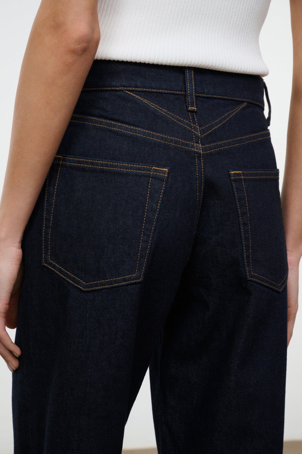 Indigo jeans showing waistband stitching, button fly, and front pocket panels.