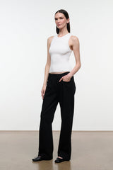 A woman modeling a white ribbed sleeveless crop top and black wide-leg trousers against a plain white studio wall.