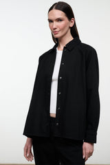 Black shirt jacket with stand collar and button placket, worn over a white top; side view.