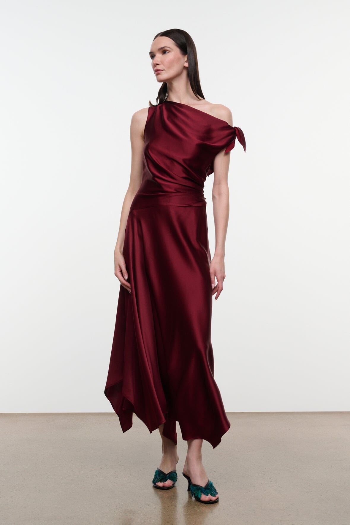 Deep burgundy silk midi dress with one-shoulder drape and flowing asymmetrical hem