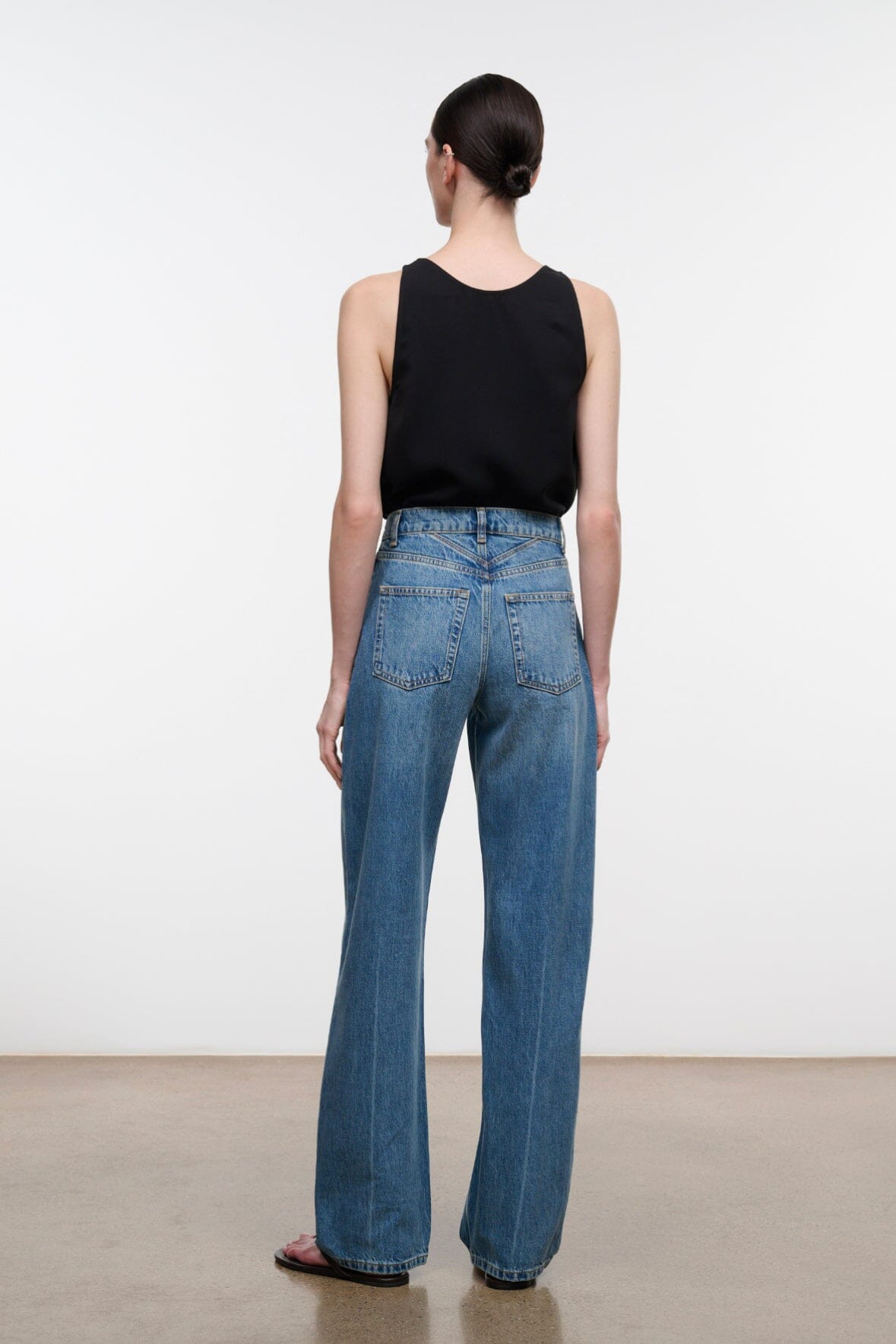 Back view: high-rise blue denim jeans with yoke and rear patch pockets.