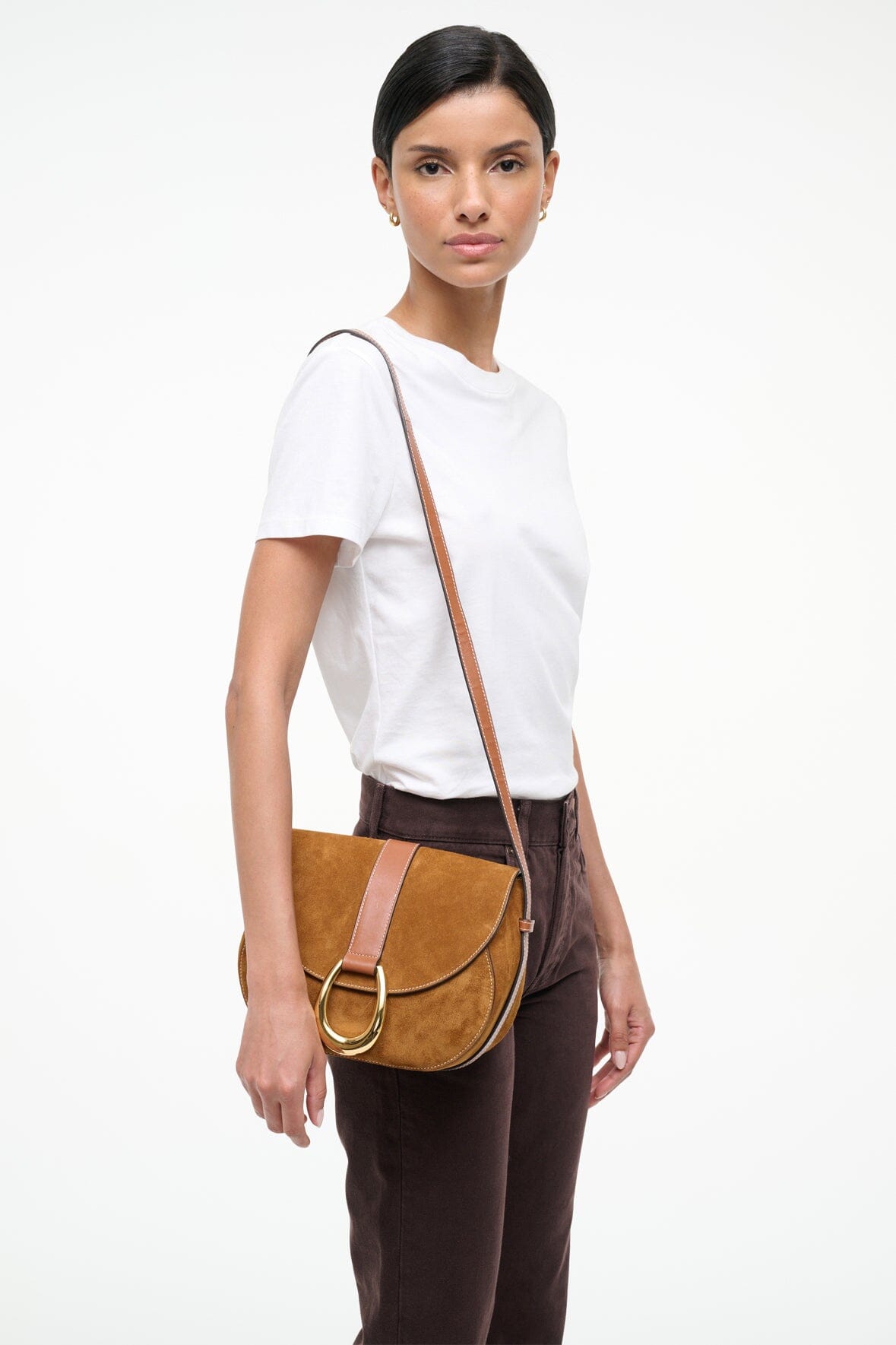 Tan suede saddle bag worn crossbody, foldover flap with gold ring hardware.
