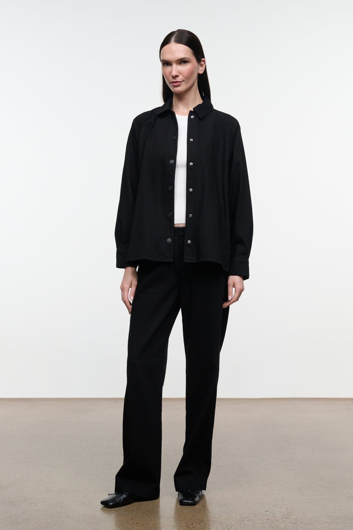 Black shirt jacket with stand collar and button front, long sleeves; paired with black pants.