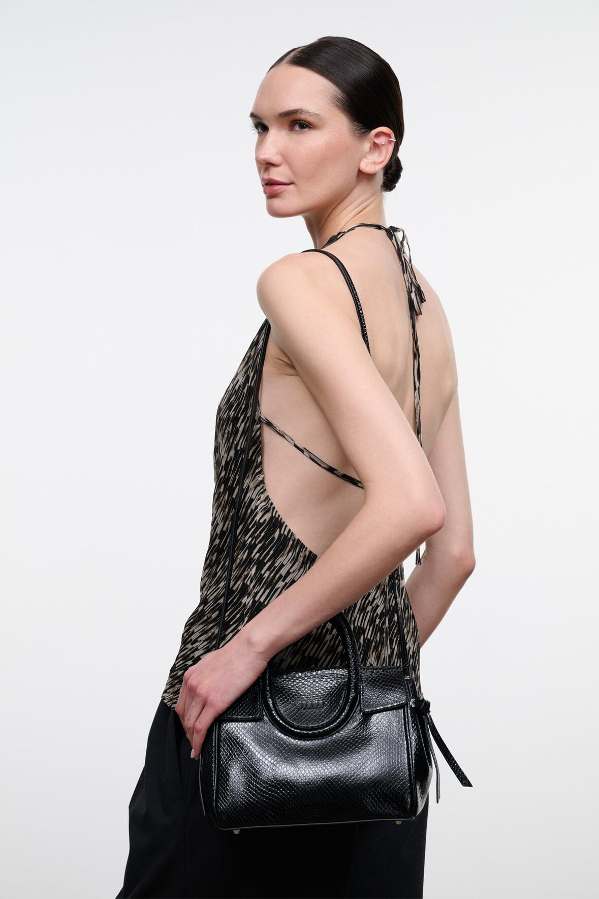Black mini carryall crossbody bag with circular textured medallion and side tassel