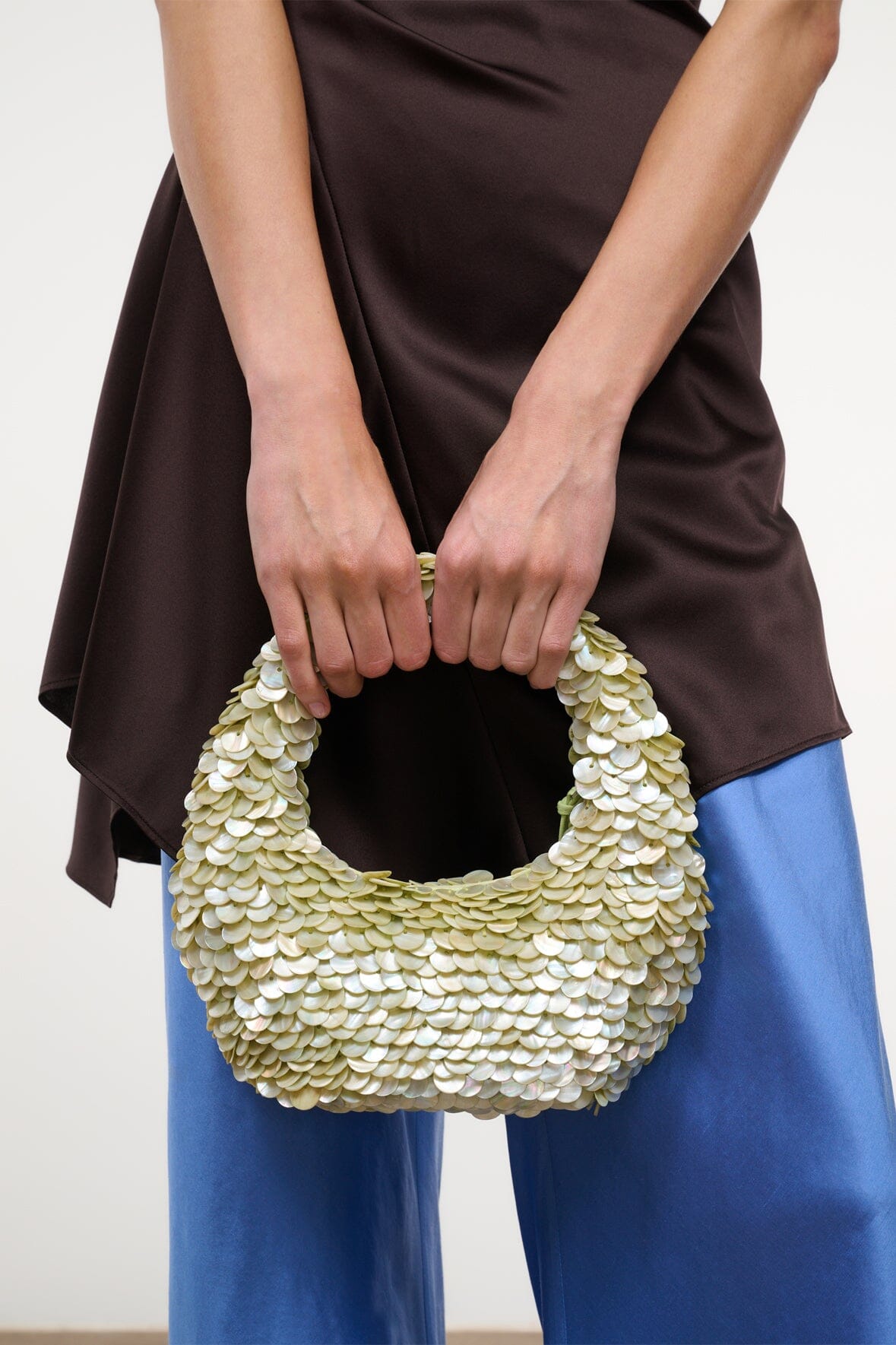 Light-green sequin-shell bag with open top and short handle, held in hands