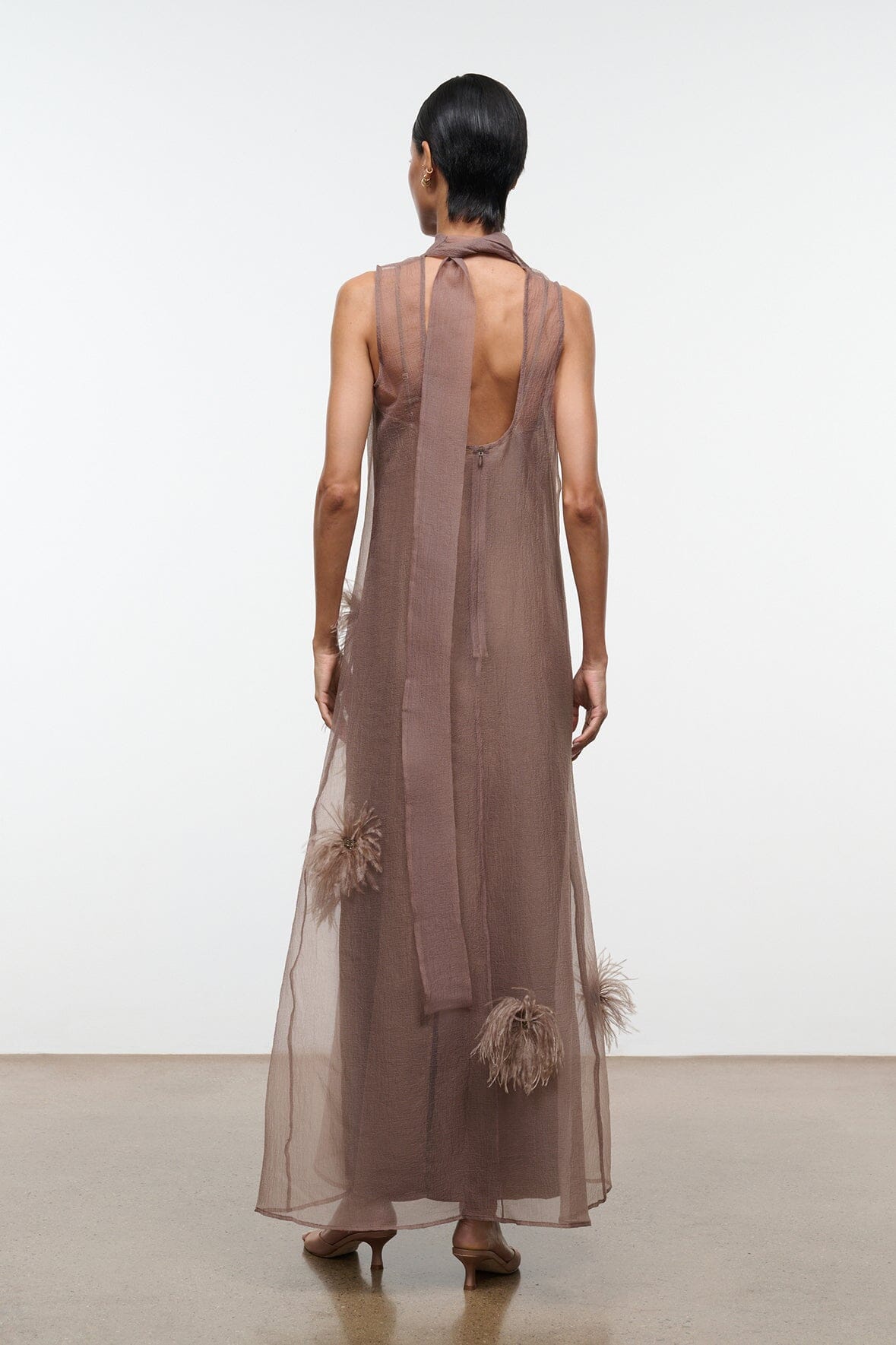 Taupe maxi dress with open back, neck tie, and feather applique accents