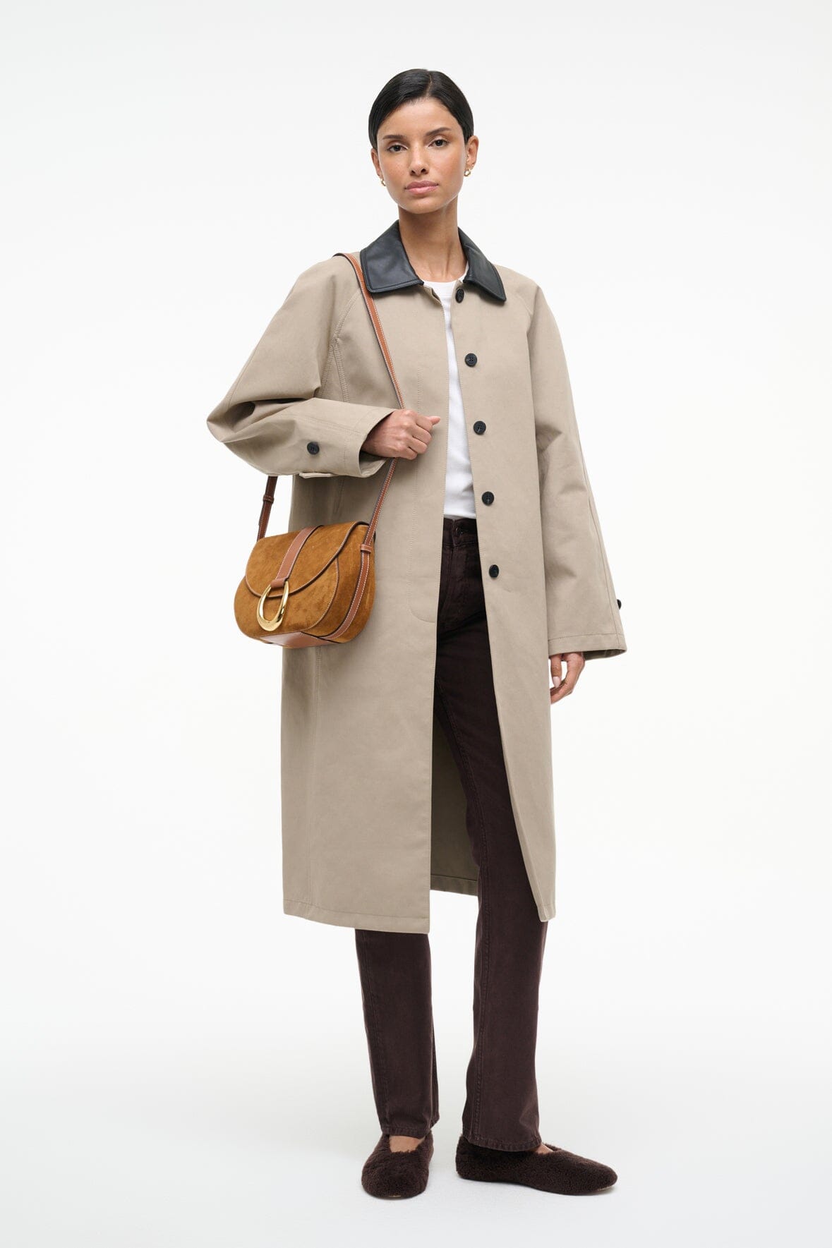 Tan suede saddle bag worn crossbody, small round gold ring on front flap.