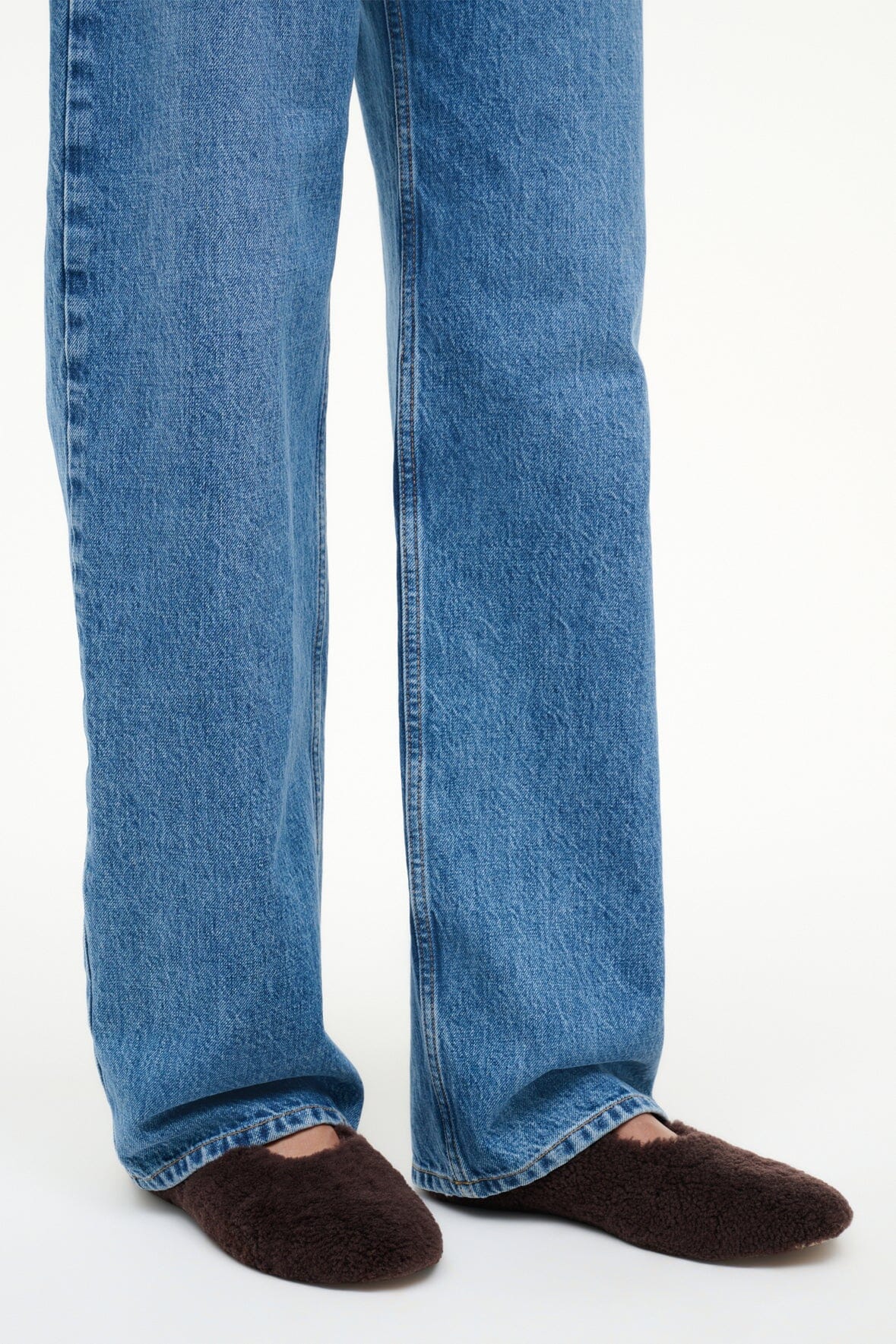 Shearling ballet flats on feet under cuffed blue jeans