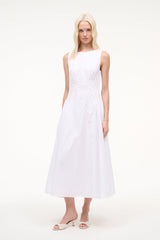 White open-toe mule sandals with textured upper and mid-height heel worn with dress