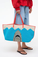 Woven tote bag with blue and natural stripes and shark-mouth graphic, red handles