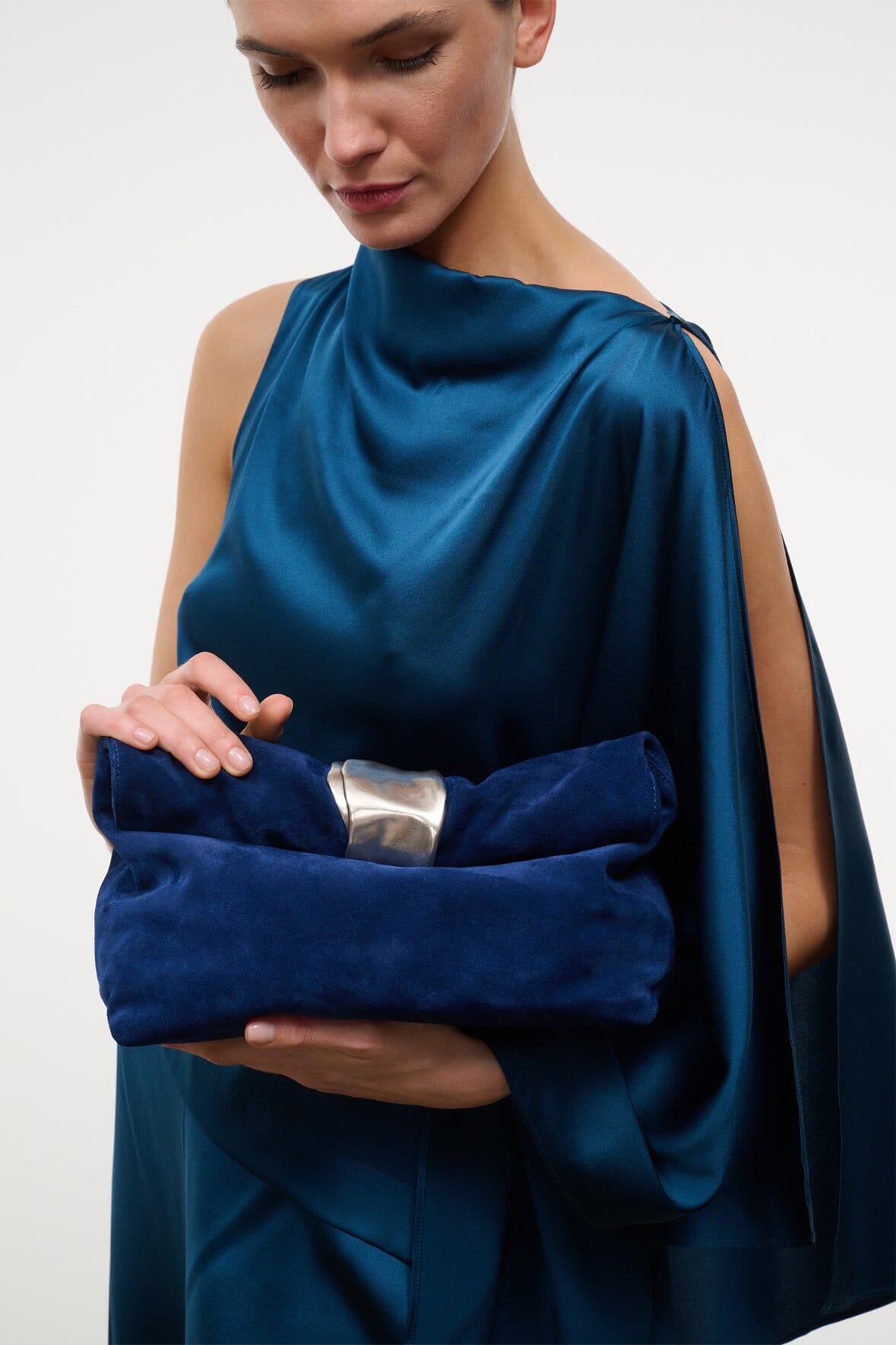 Cobalt suede cuff clutch with silver-tone clasp, held close to chest