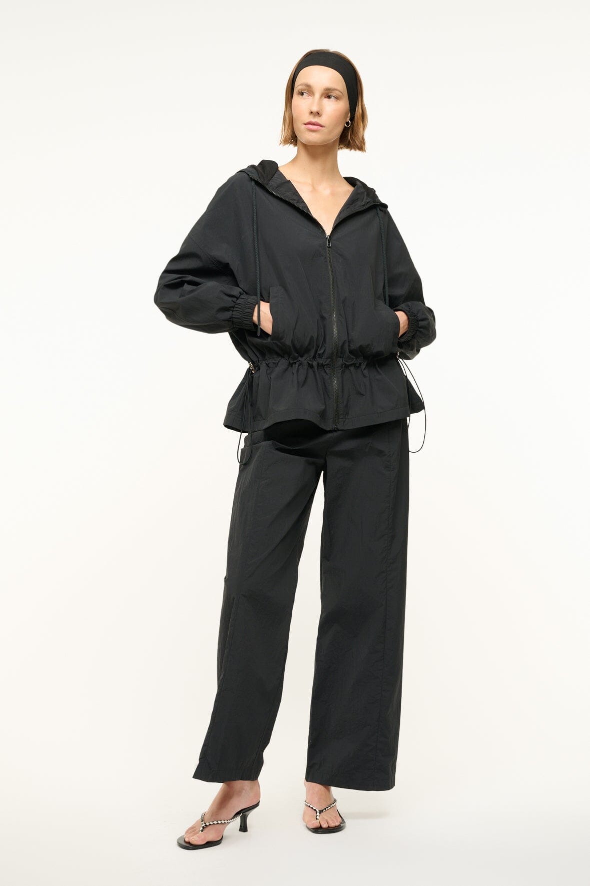 Black hooded jacket with zip front, roomy sleeves, and gathered waist detail.