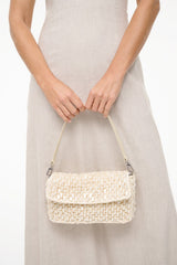 Cream woven shoulder bag worn at waist height with flap closure