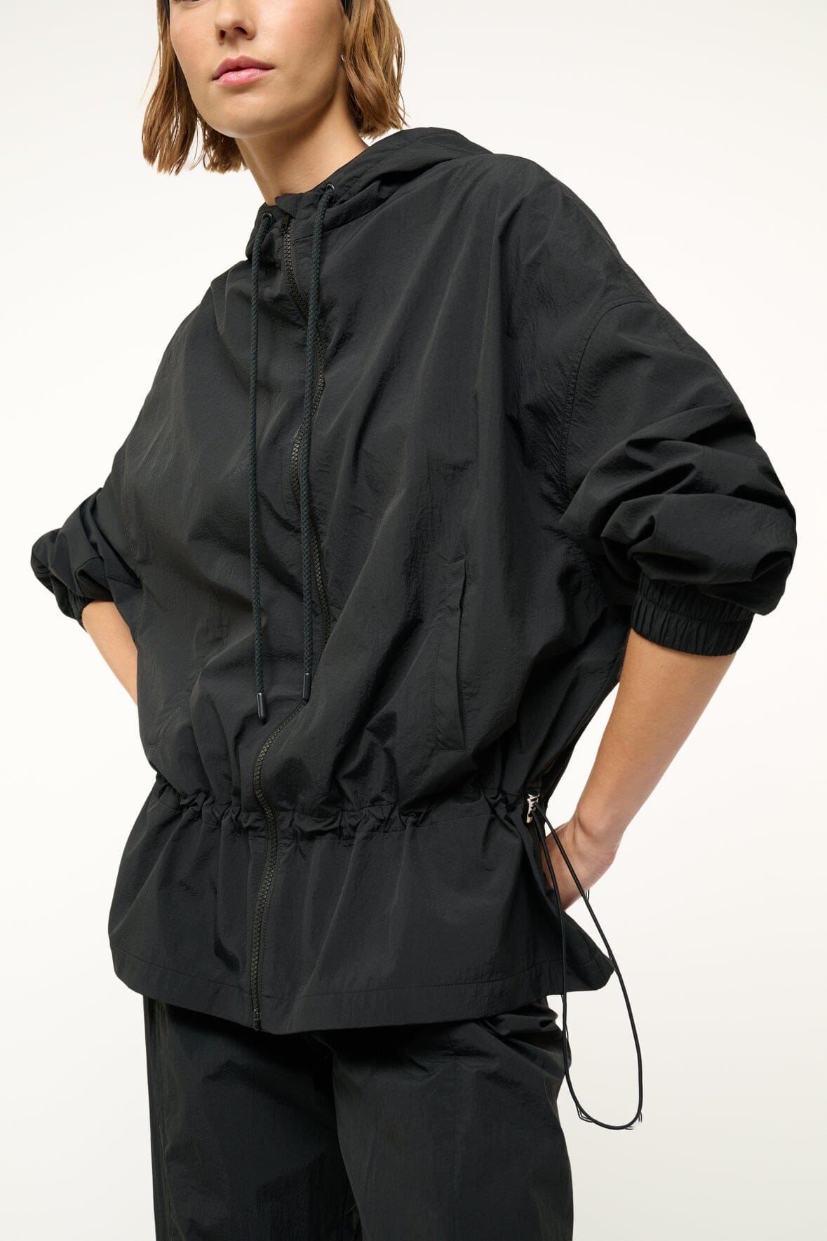 Black hooded jacket with front zipper, elastic cuffs, and gathered drawstring waist.
