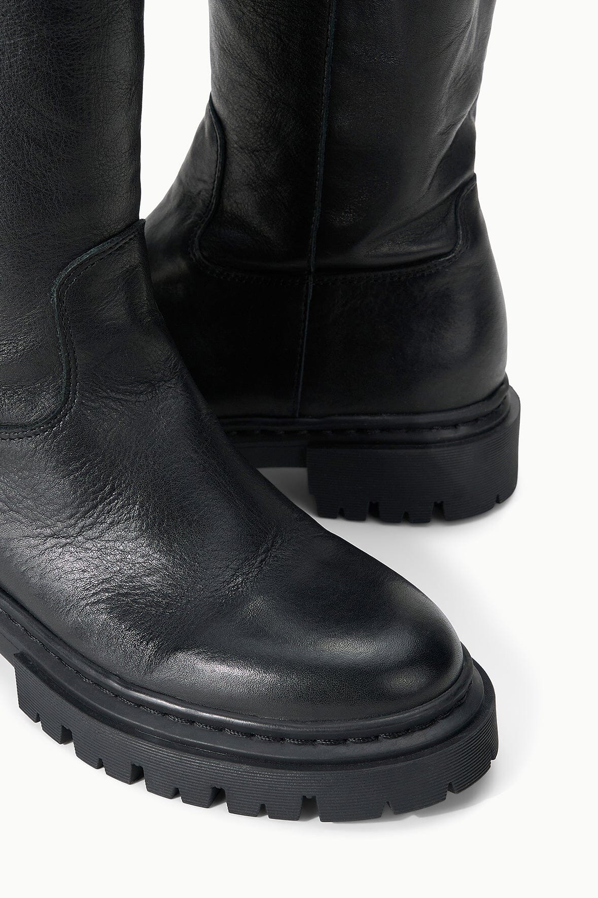 Black tall leather boot detail with stitched ankle seam and lug tread sole