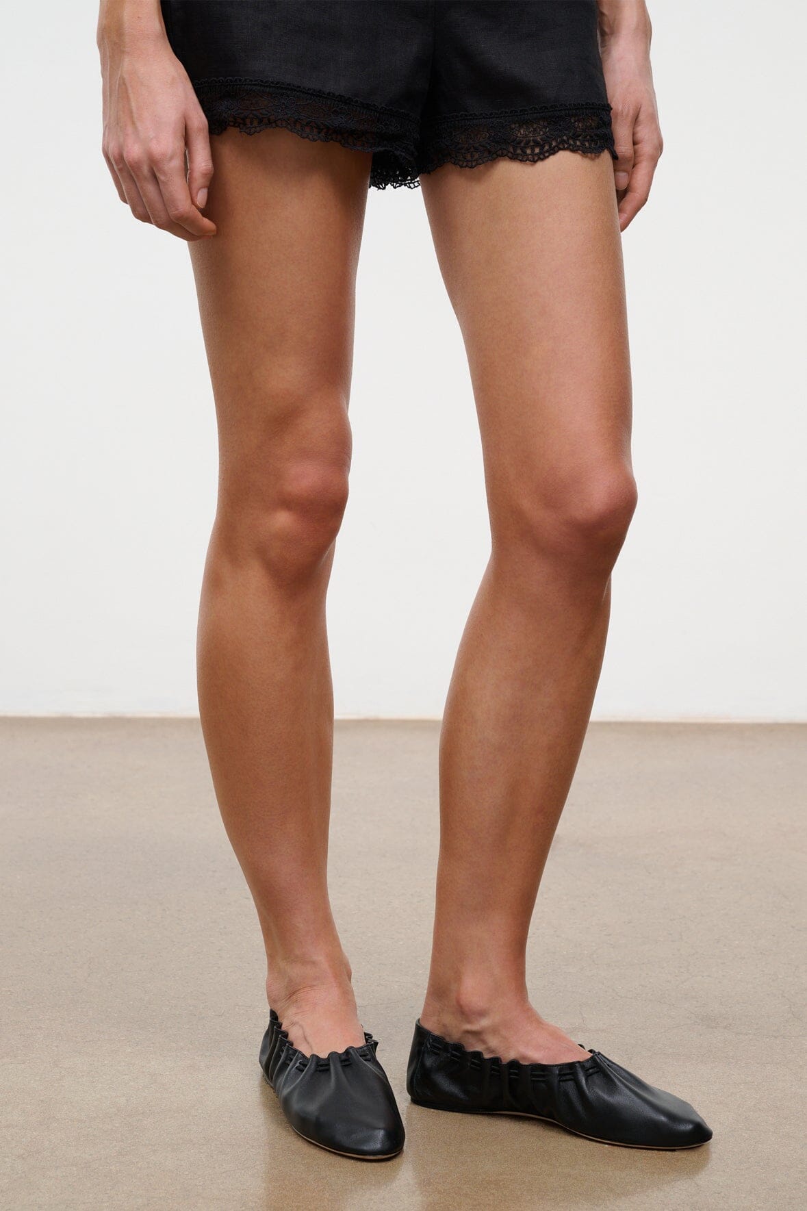 Black flat sneakers with rounded toe, worn with black lace-trim shorts