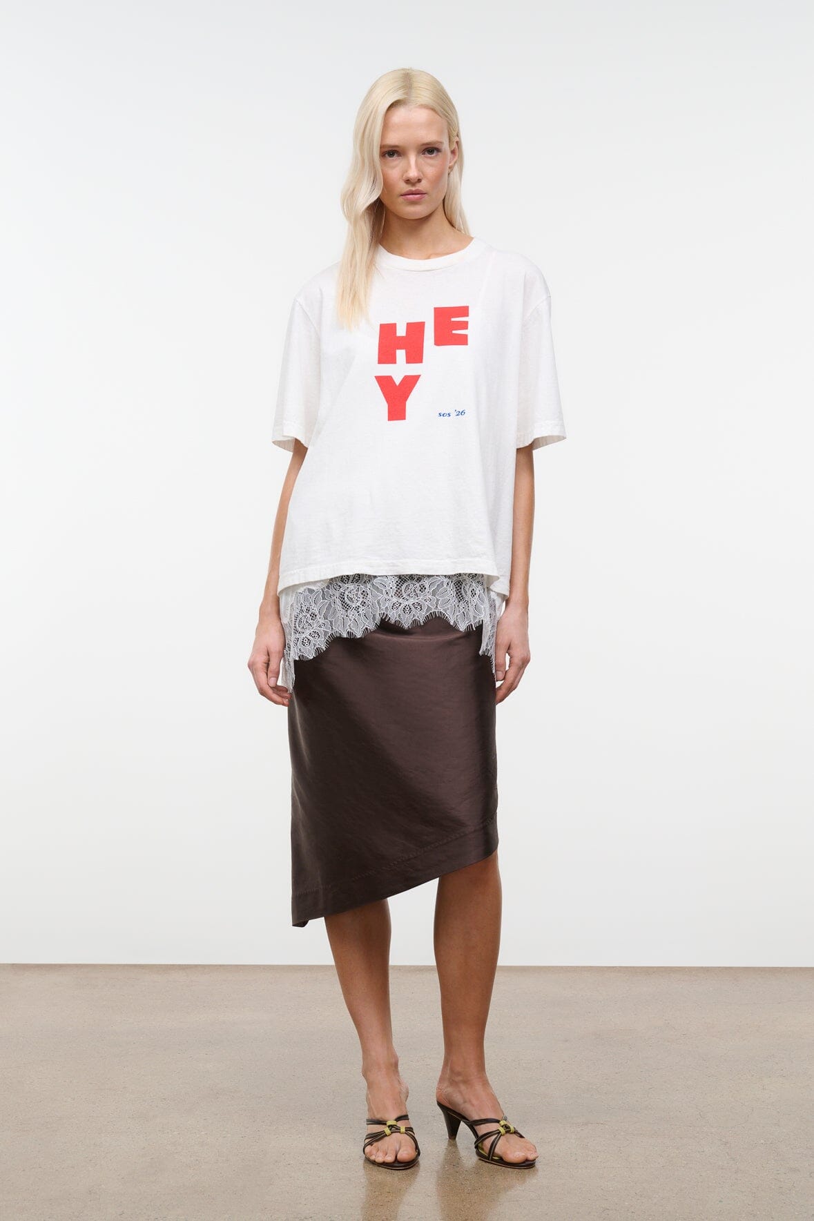 White relaxed tee with red “HEY” graphic; worn with a dark brown skirt.