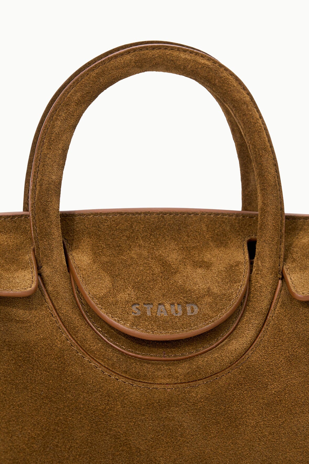 Cigar-brown handbag front with STAUD logo on circular patch beneath the handle.