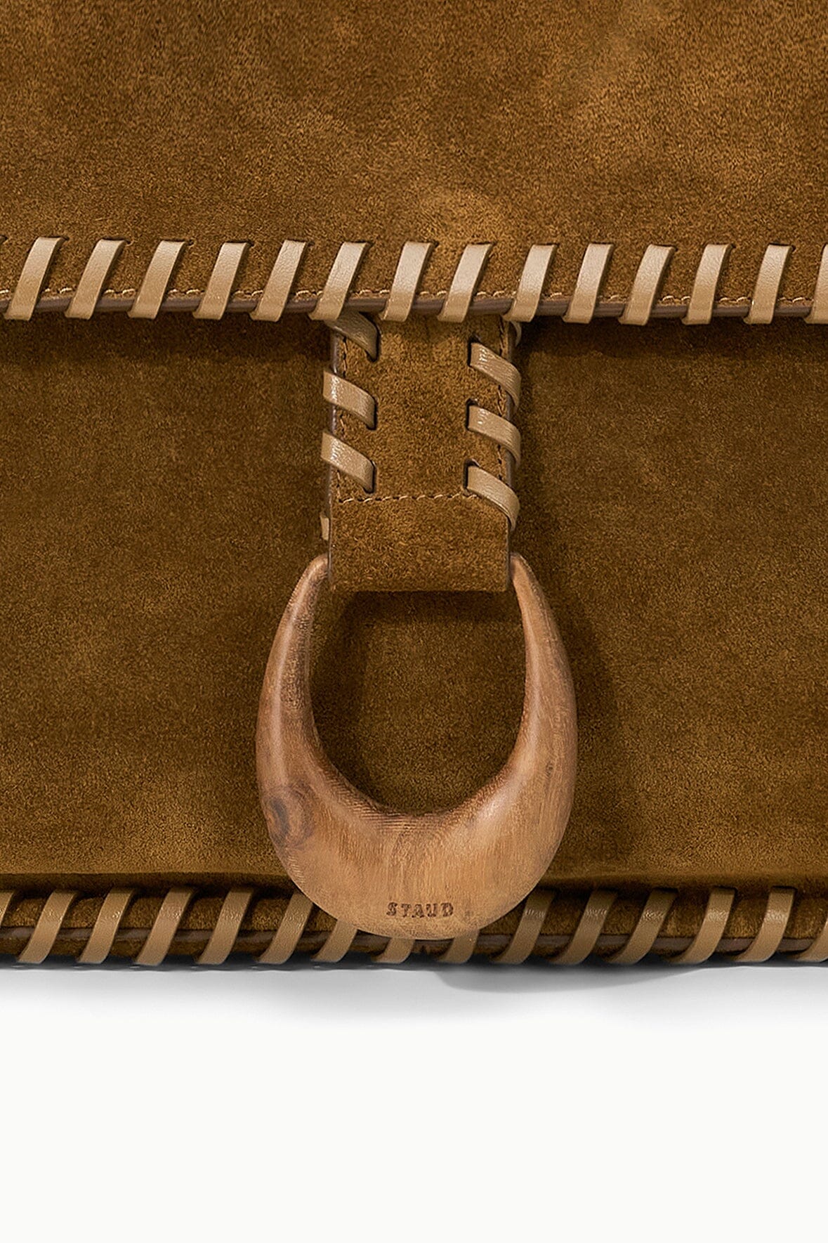 Harlow messenger bag close-up: cigar-brown suede flap with circular buckle hardware