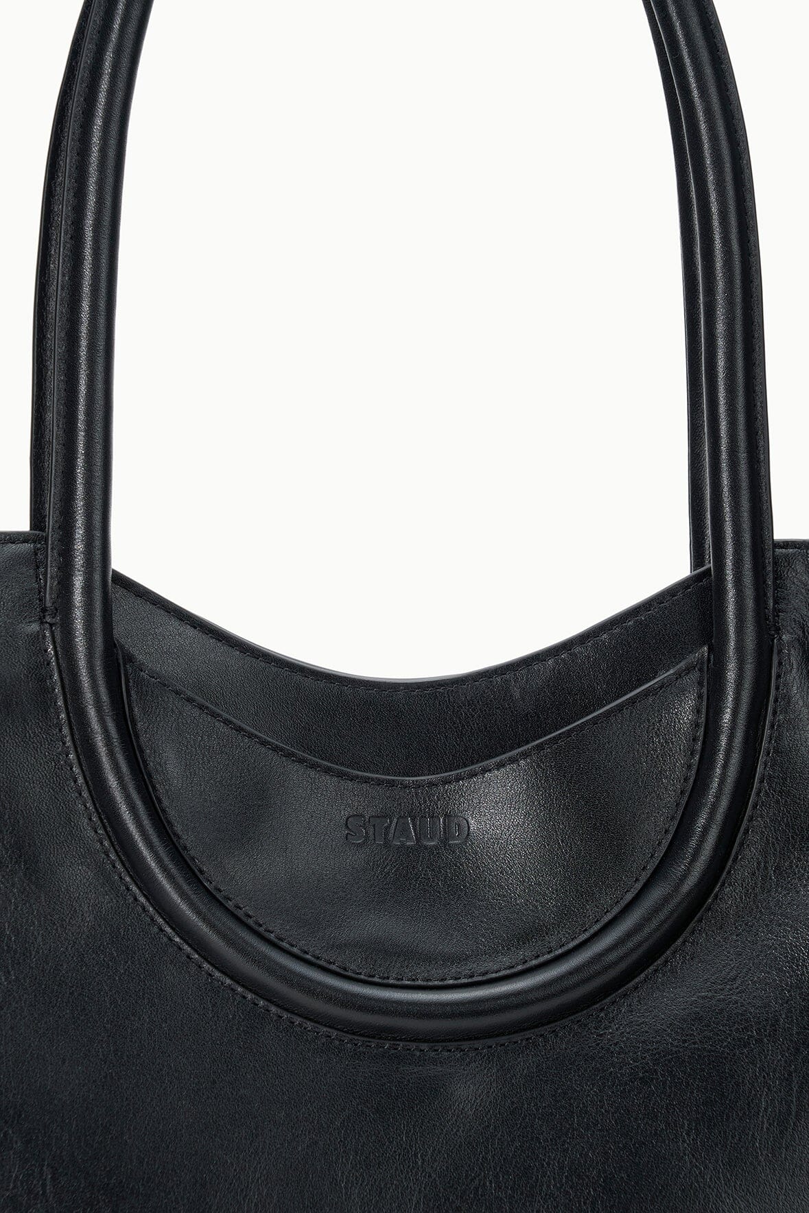 MAUDE black north-south tote, close-up of curved handle opening with embossed logo