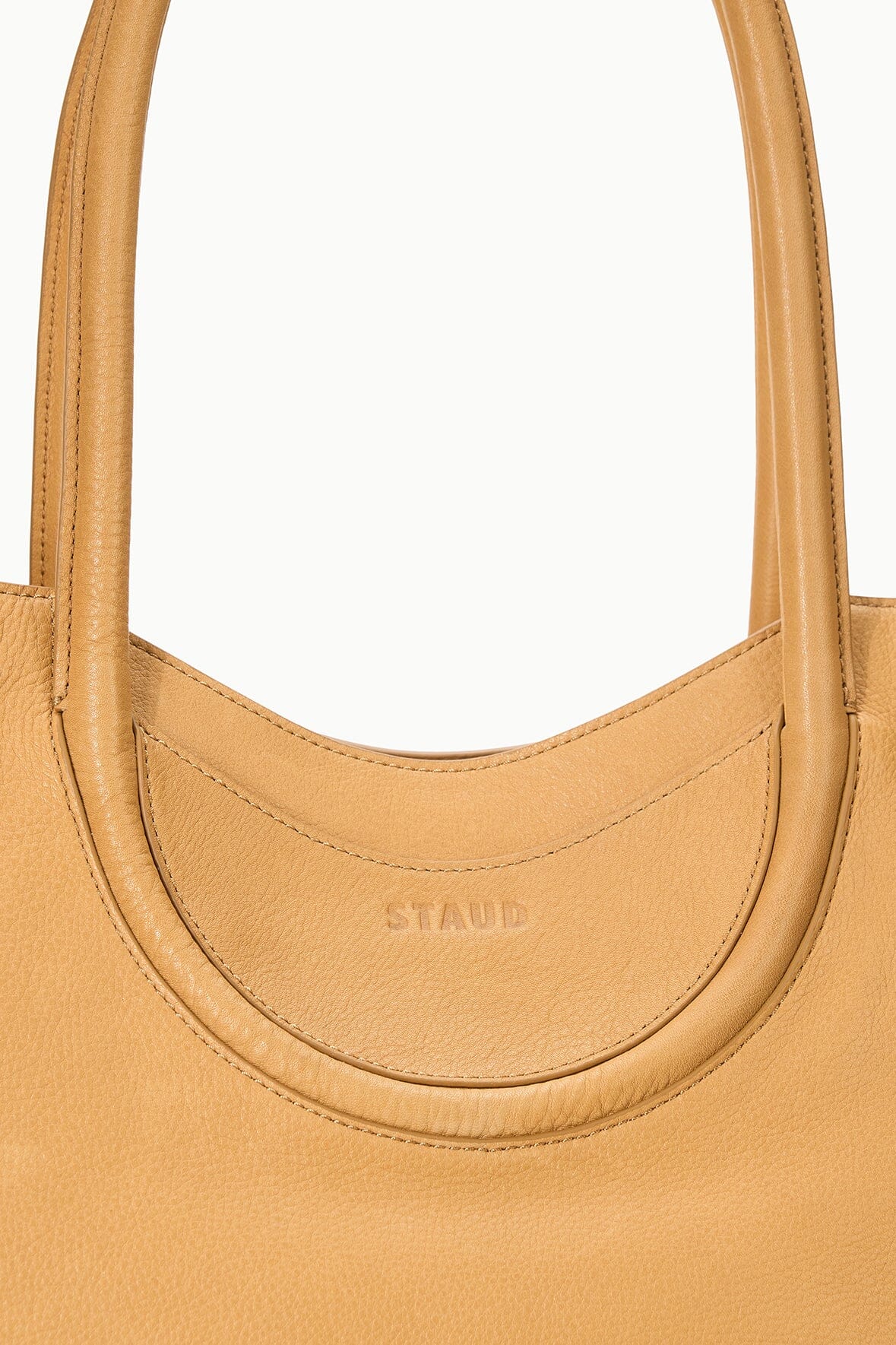 Tan tote with curved neckline and embossed brand mark at the handle base
