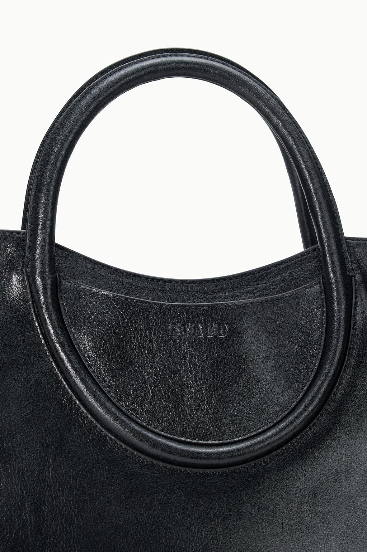 Maude black satchel close-up: oval handle base with stamped logo