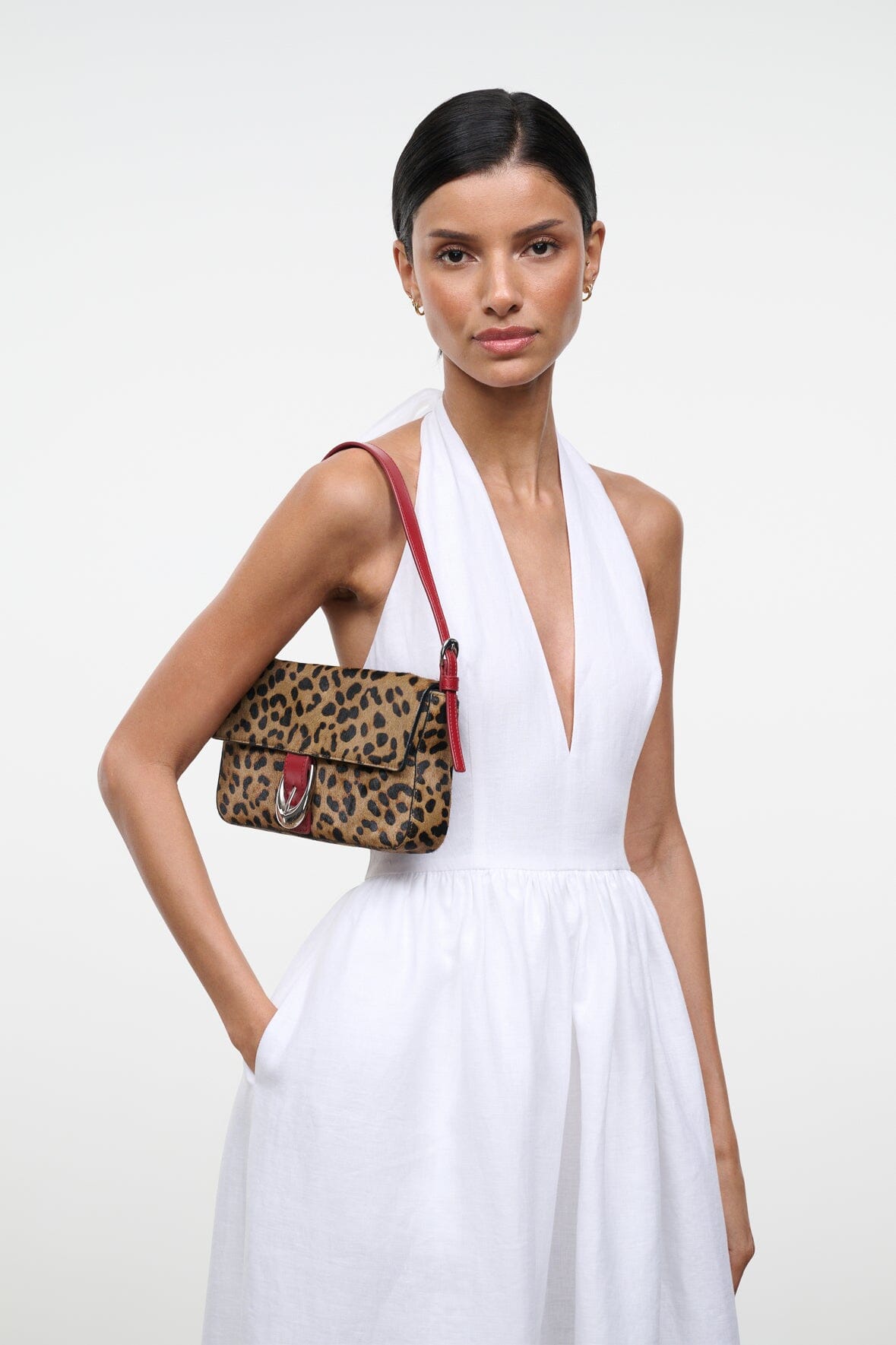 Cheetah-print flap shoulder bag with red strap and silver buckle, side view on model