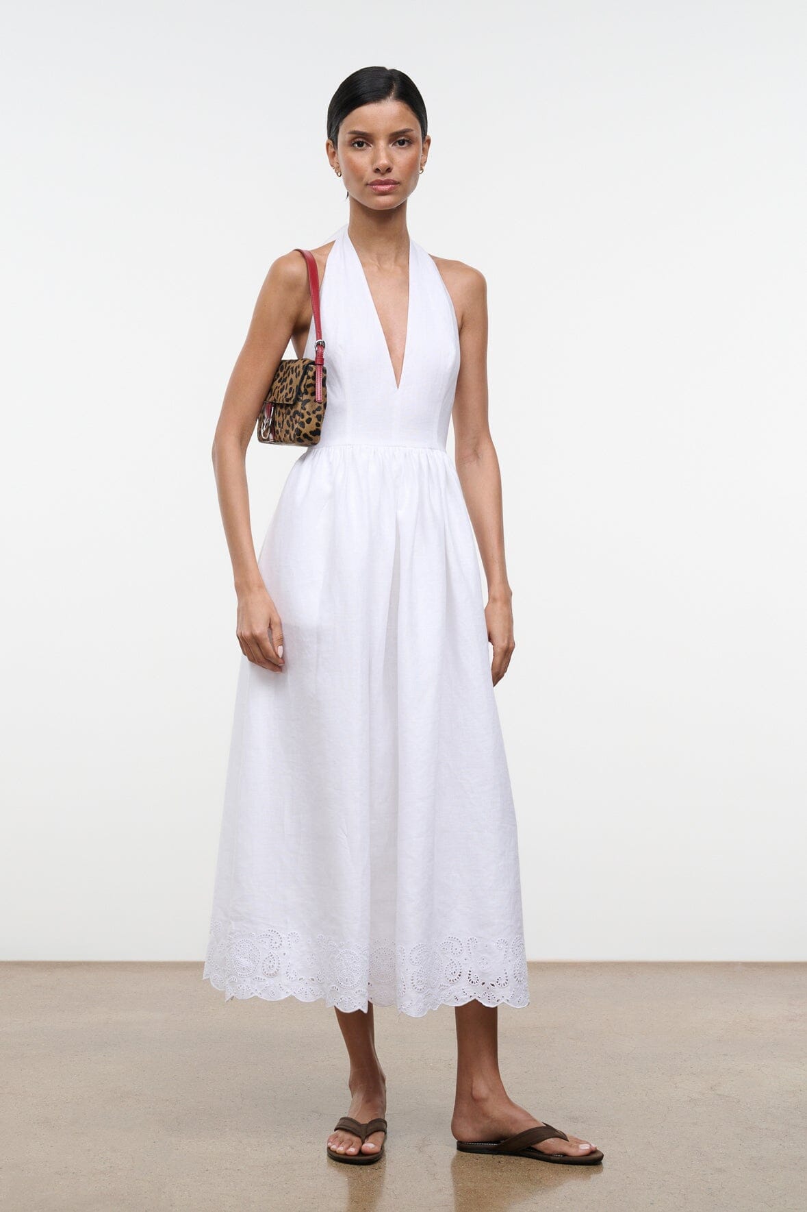 Cheetah-print shoulder bag with red strap and silver buckle, worn by model in white dress