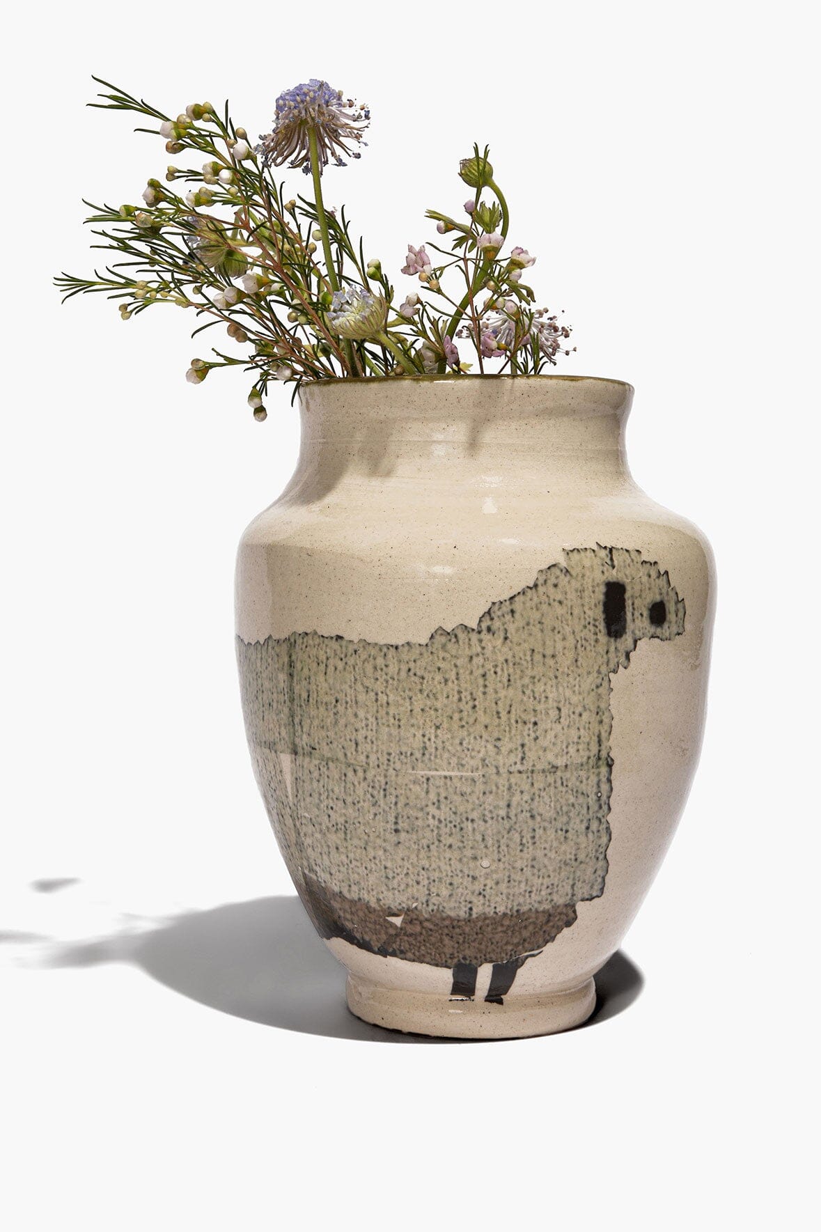 Round ceramic sheep vase with beige body, black sheep silhouette, holding small flowers