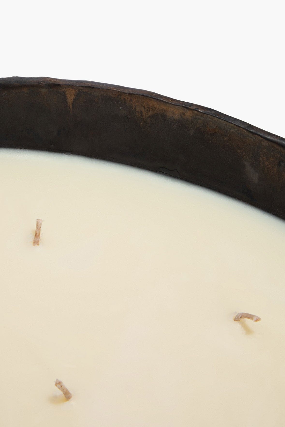 White wax surface with wick ends inside dark ceramic candle bowl