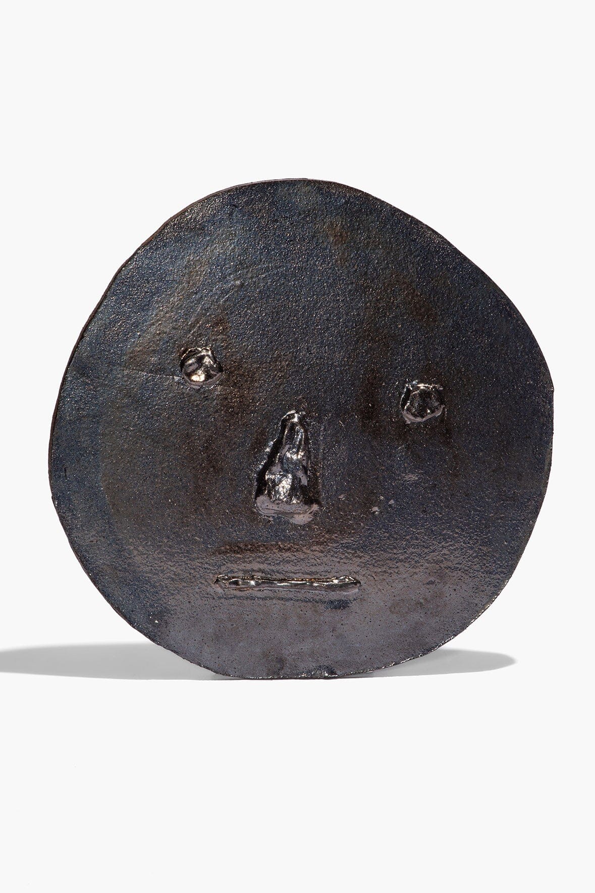 Ceramic face ornament in dark burnt black glaze, round with embossed facial features