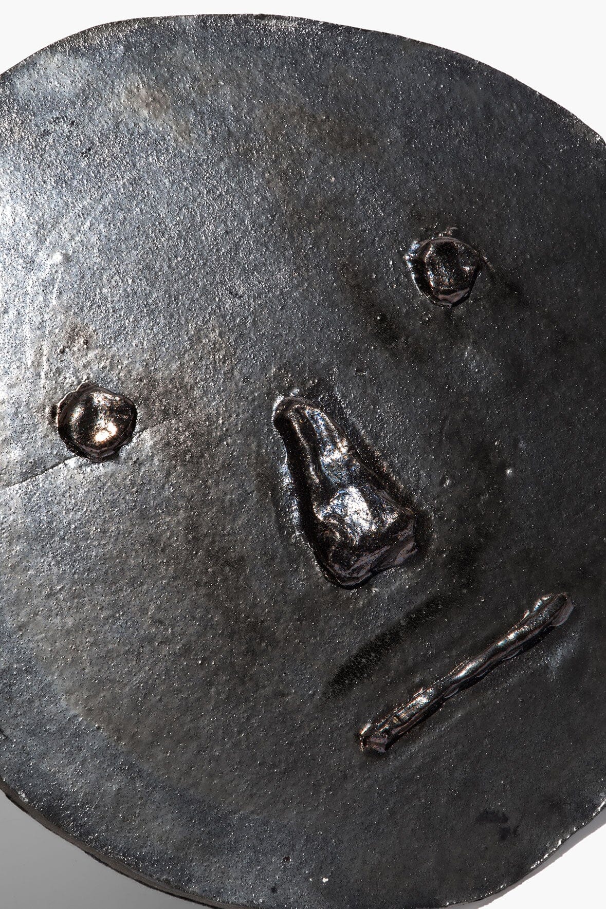 Round ceramic face ornament close-up in dark burnt black glaze with embossed details