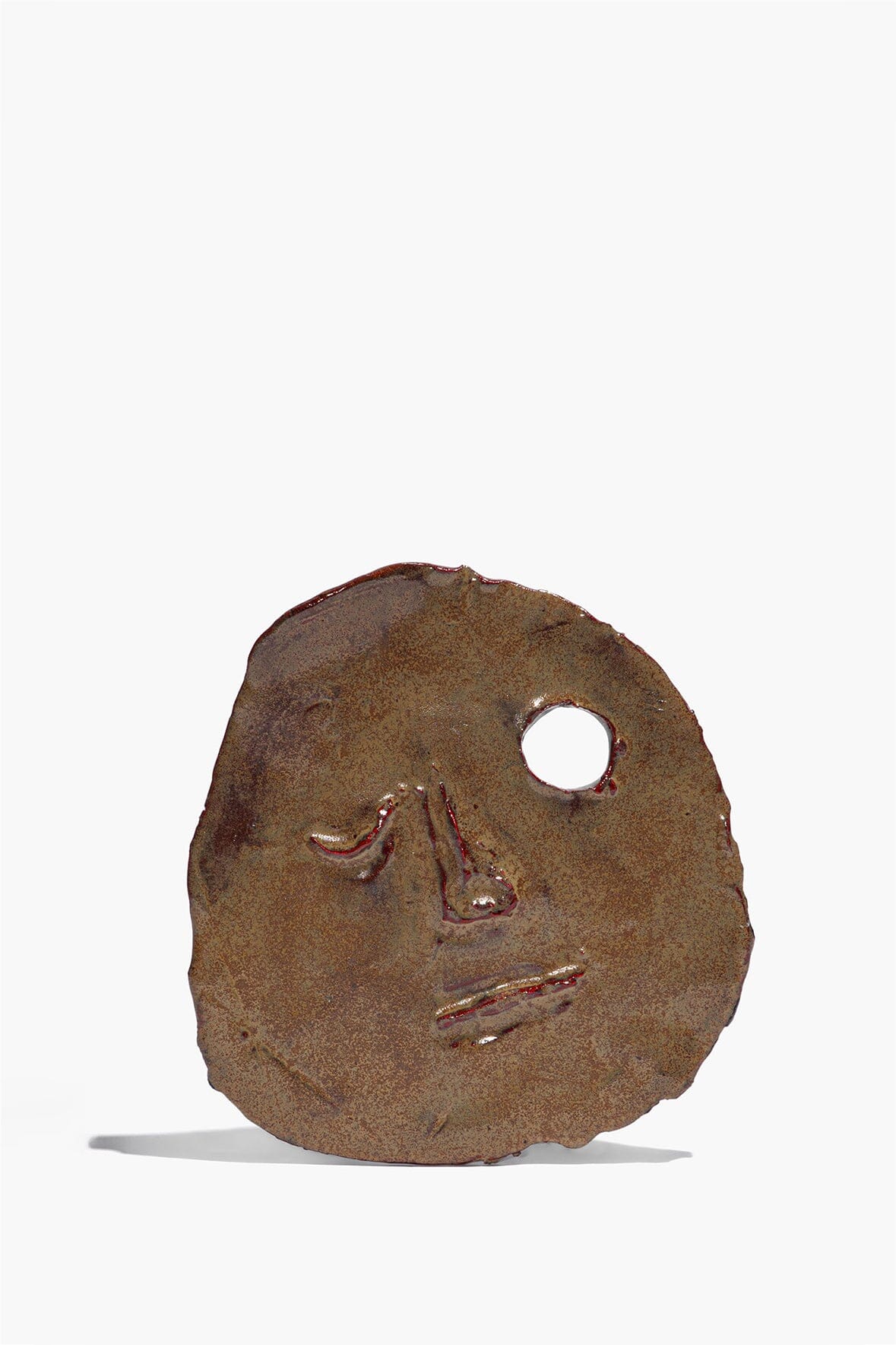 Ceramic face ornament in molasses brown glaze with round hole and painted eyes.