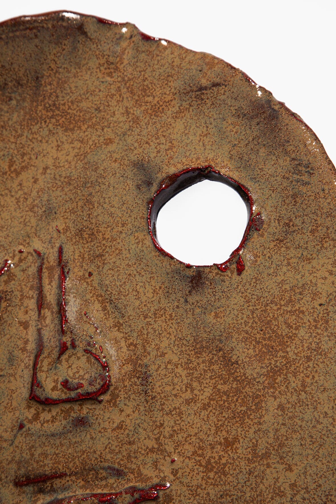 Ceramic face ornament detail: circular hole and painted nose/mouth on dark brown glaze.