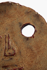 Ceramic face ornament detail: circular hole and painted nose/mouth on dark brown glaze.