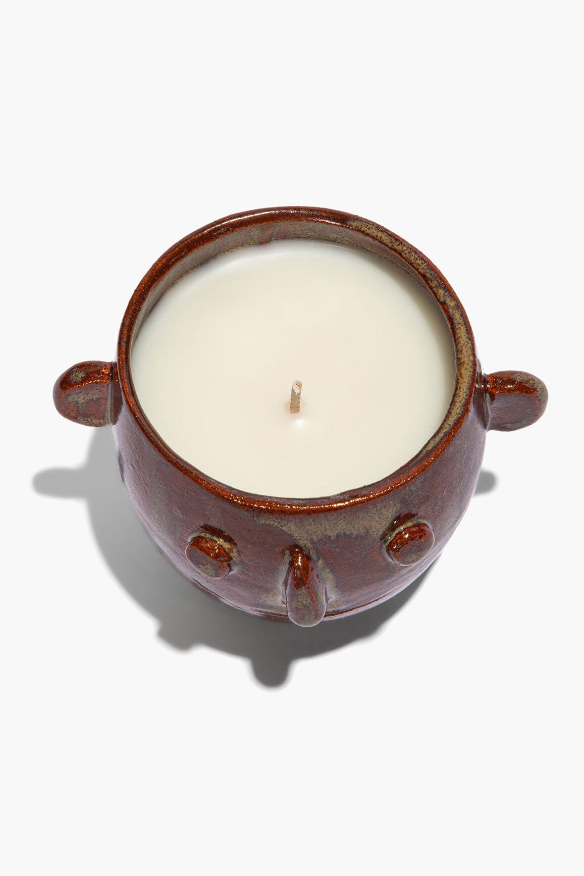 Ceramic candle pot viewed from top, brown rim and side handles; white wax with wick