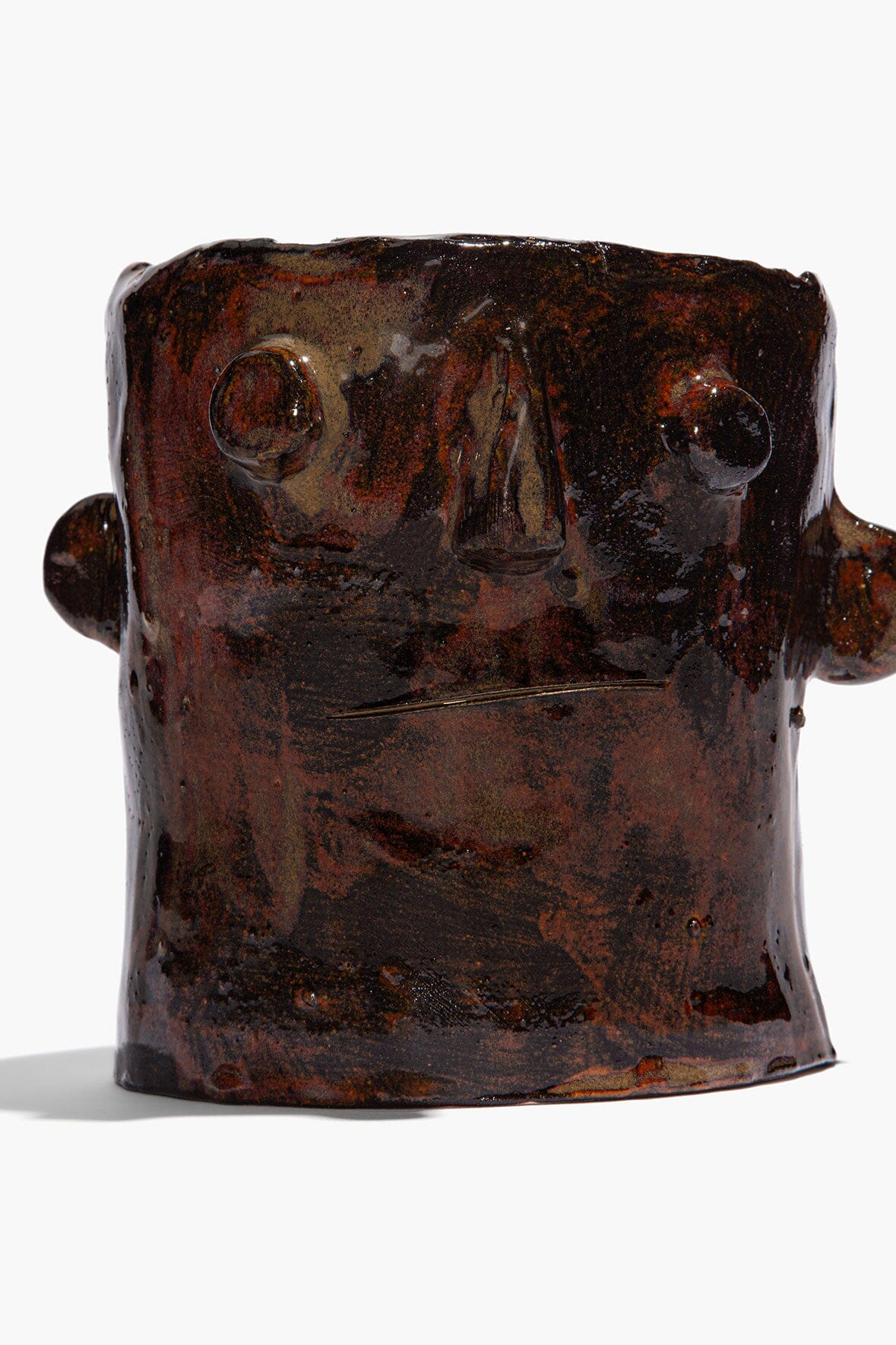 Brown ceramic candle holder with sculpted face and side knobs, wide open top