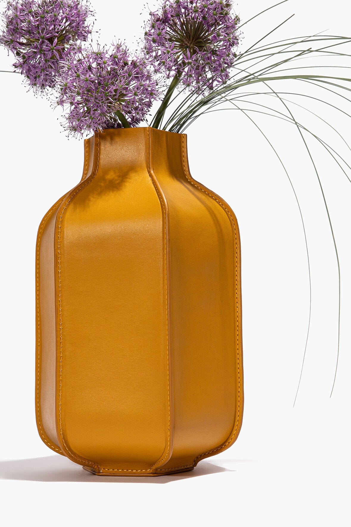 Goldenrod leather bottle vase with open neck holding purple dried flowers