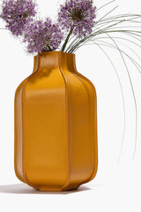 Goldenrod leather bottle vase with open neck holding purple dried flowers