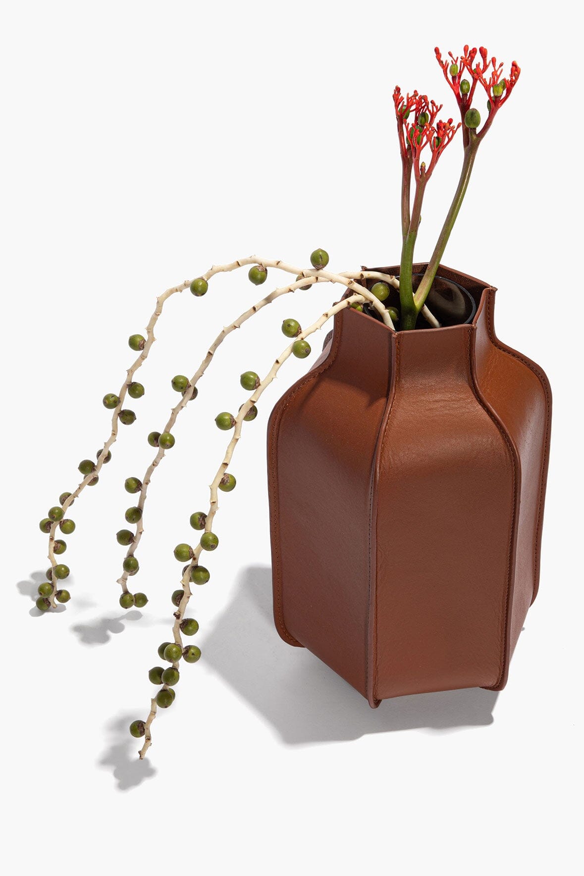 Tan leather bottle vase with cutout handle shape holding stems and flowers