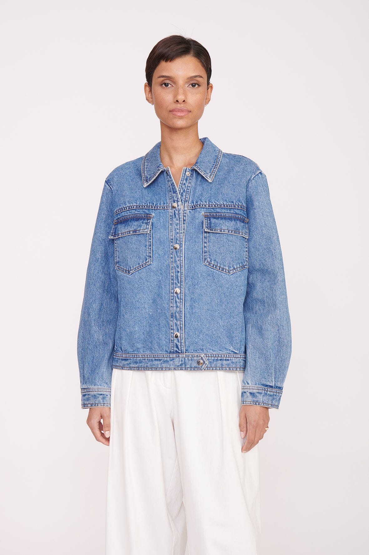 Medium-wash denim jacket with button front and flap chest pockets, visible seams