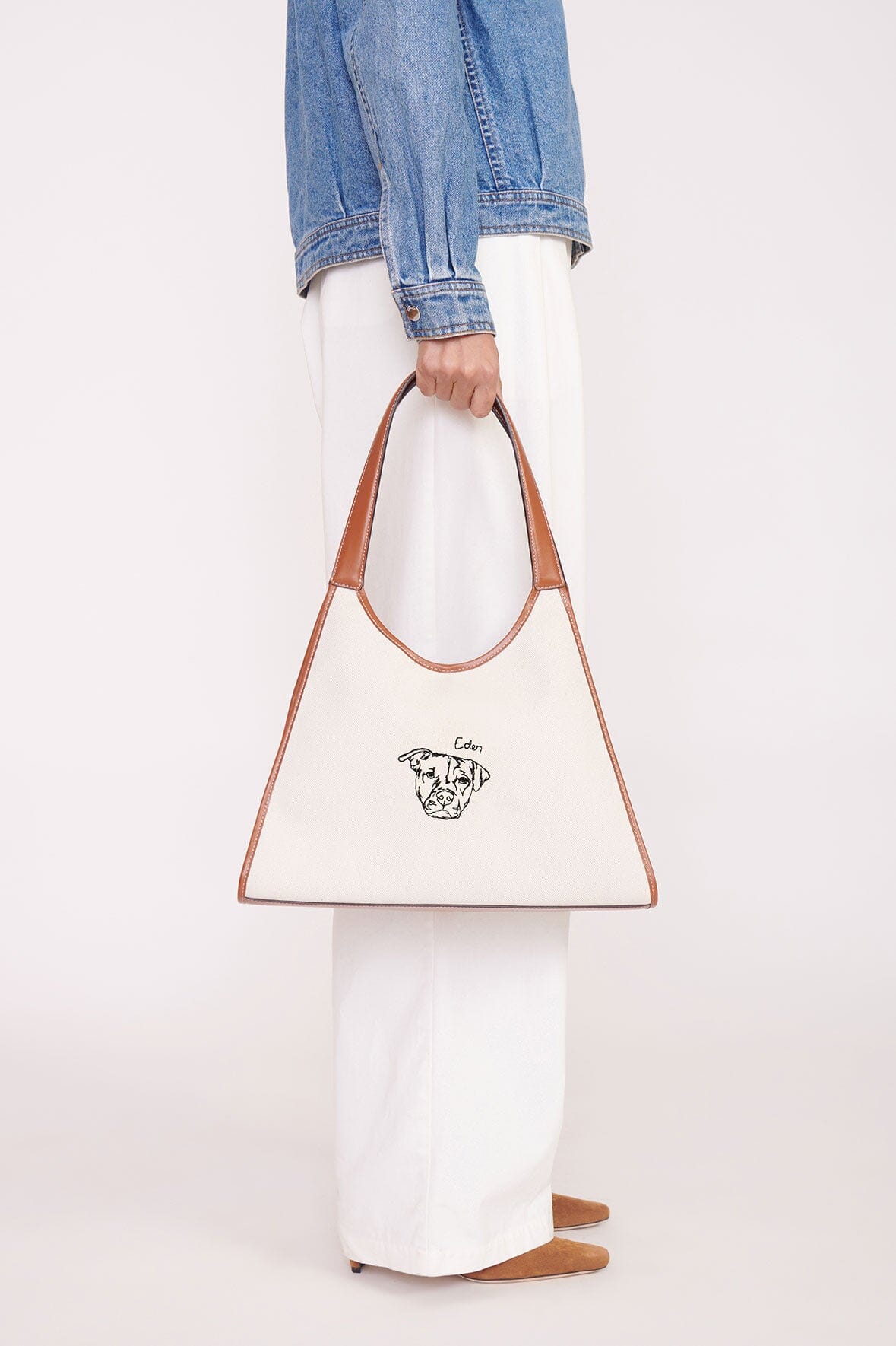 Cream canvas tote bag with tan leather handles and illustrated dog logo