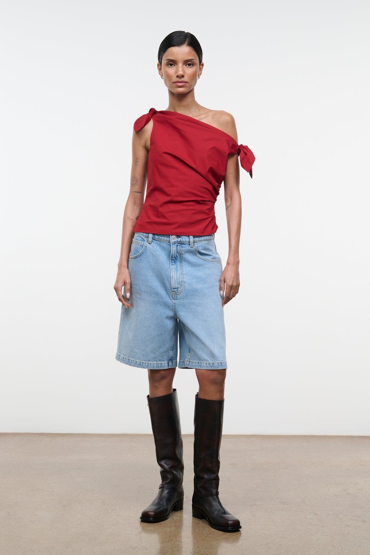 Red asymmetrical one-shoulder draped top with tied bow detail at the shoulder.