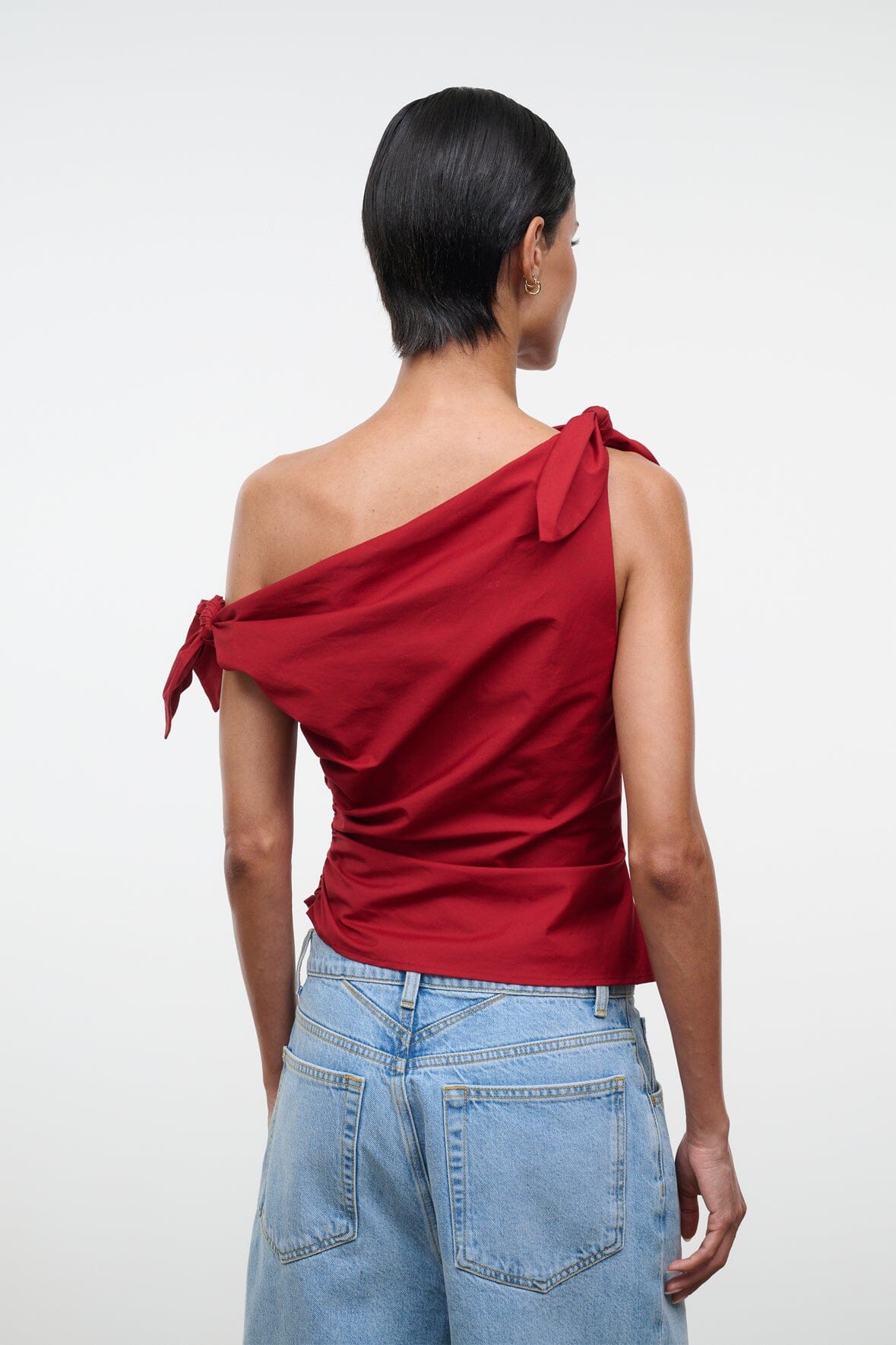 Back view of red asymmetrical one-shoulder draped top with bow tie at shoulder.
